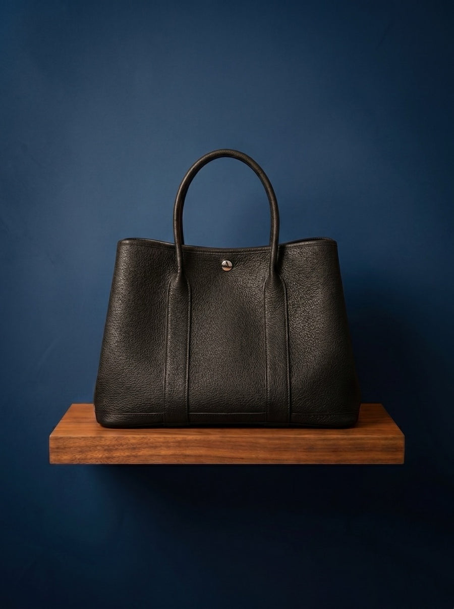 Hermès Garden Party PM Handbag Black leather handbag on a wooden stand against a blue background